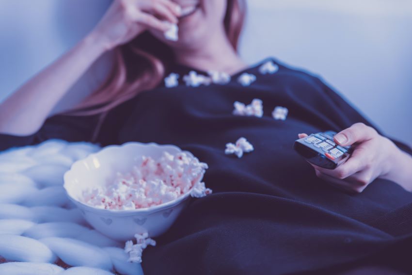 woman eating popcorn while holding the remote