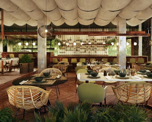 A cozy, modern restaurant with green and wicker chairs, wooden tables, and hanging globe lights. The ceiling has cloud-like panels, creating a welcoming ambiance.