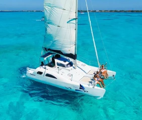 Arial view of a catamaran boat sailing on turquoise water with people sitting on the boats edge.
