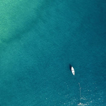 A small white boat floats on vast, calm blue-green water, casting a shadow beneath.