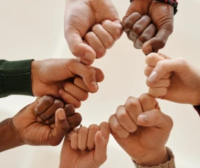 Eight diverse hands forming a circle with pinky fingers interlocked. The image conveys unity and teamwork against a neutral background.