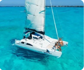 Arial view of a catamaran boat sailing on turquoise water with people sitting on the boats edge.