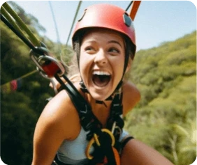 A person with a red helmet smiles widely while zip-lining through lush green forest. The image captures excitement and adventure.
