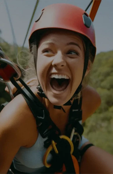 A person with a red helmet smiles widely while zip-lining through lush green forest. The image captures excitement and adventure.