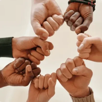 Eight diverse hands forming a circle with pinky fingers interlocked. The image conveys unity and teamwork against a neutral background.