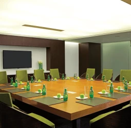 Modern resort boardroom with a large square wooden table, green chairs, and flat-screen TV.