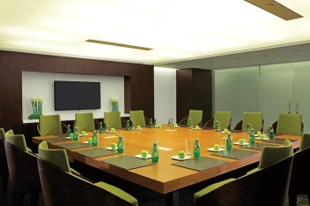 Modern resort boardroom with a large square wooden table, green chairs, and flat-screen TV.