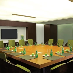 Modern resort boardroom with a large square wooden table, green chairs, and flat-screen TV.