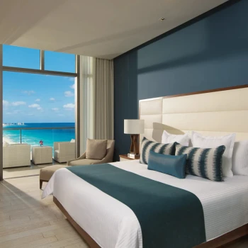 Deluxe ocean view king suite bedroom with blue accents and a private balcony overlooking the sea.