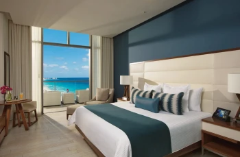 Deluxe ocean view king suite bedroom with blue accents and a private balcony overlooking the sea.