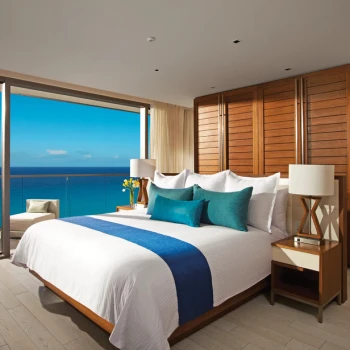 Bright Master Suite with a king bed, warm wood accents, and a wide balcony overlooking the ocean.