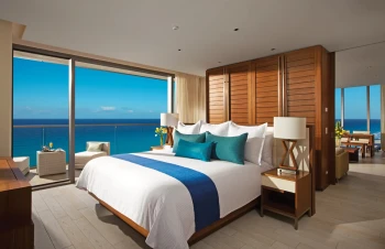 Bright Master Suite with a king bed, warm wood accents, and a wide balcony overlooking the ocean.