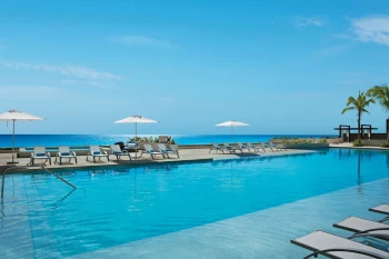 Resort pool area with lounge chairs under umbrellas and the bright blue Caribbean Sea in the background.