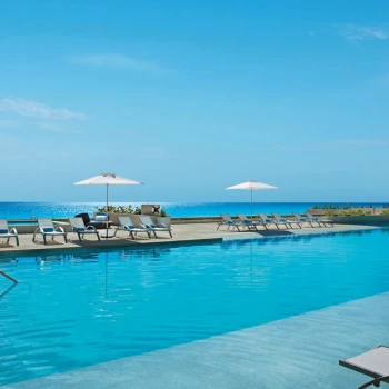 Resort pool area with lounge chairs under umbrellas and the bright blue Caribbean Sea in the background.