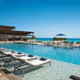 Infinity pool with a deck of lounge chairs, a shaded bar area, and an expansive ocean view.