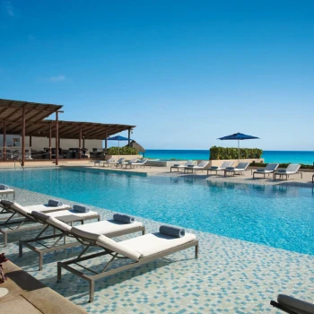 Infinity pool with a deck of lounge chairs, a shaded bar area, and an expansive ocean view.