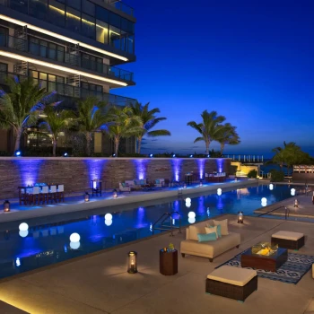 Elegant poolside event at night with blue uplighting, palm trees, and illuminated floating orbs.