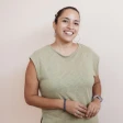Smiling woman standing against a light beige background, wearing a sleeveless green top.