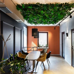 Modern conference room with a long wooden table, colorful chairs, a green foliage ceiling, and an orange accent wall.